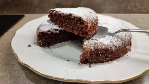 Una fetta di torta all'acqua al cacao, soffice e spolverata di zucchero a velo, viene sollevata da una paletta.