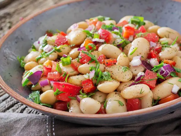 Insalata di fagioli bianchi, pomodori, cipolla rossa e erbe fresche in una ciotola rustica. Un piatto colorato e saporito.