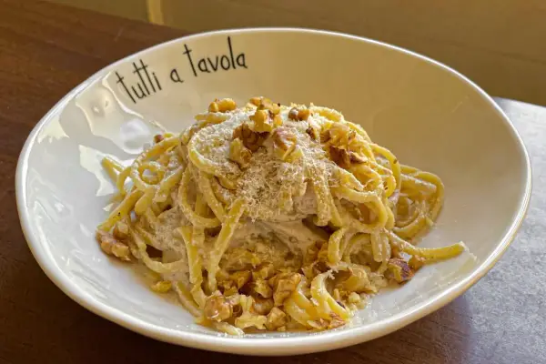 Pasta cremosa con pesto di noci, guarnita con noci tritate e parmigiano grattugiato. Un piatto invitante per tutti a tavola.